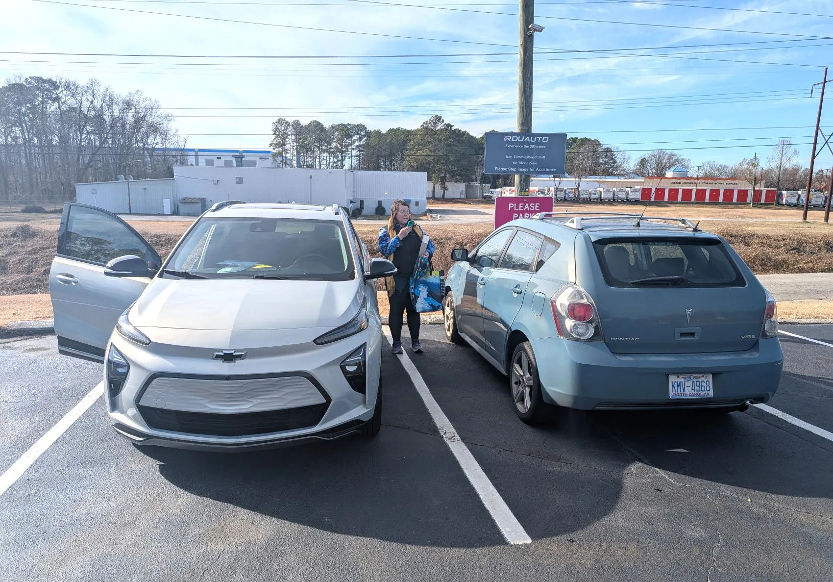 A silver Chevy Bolt EUV alongside a teal Pontiac Vibe. My wife Holly stands between them, looking lovingly at the Vibe.